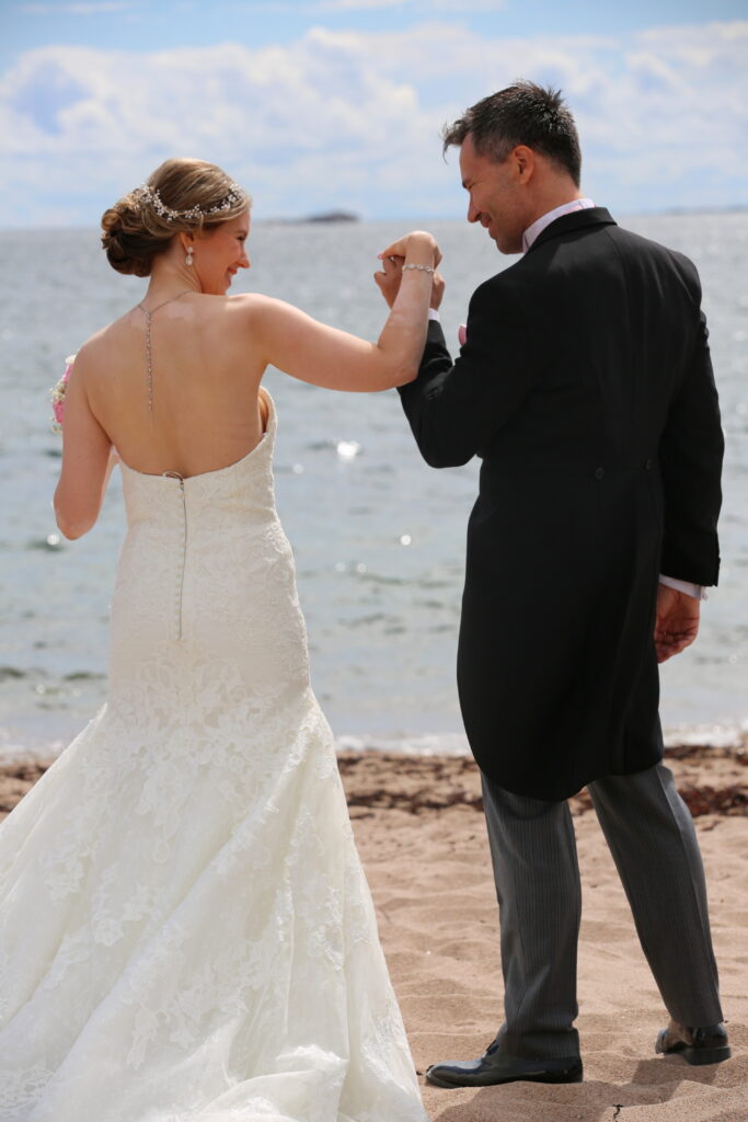 Groom in a morning coat holds his bride's hand by the sea